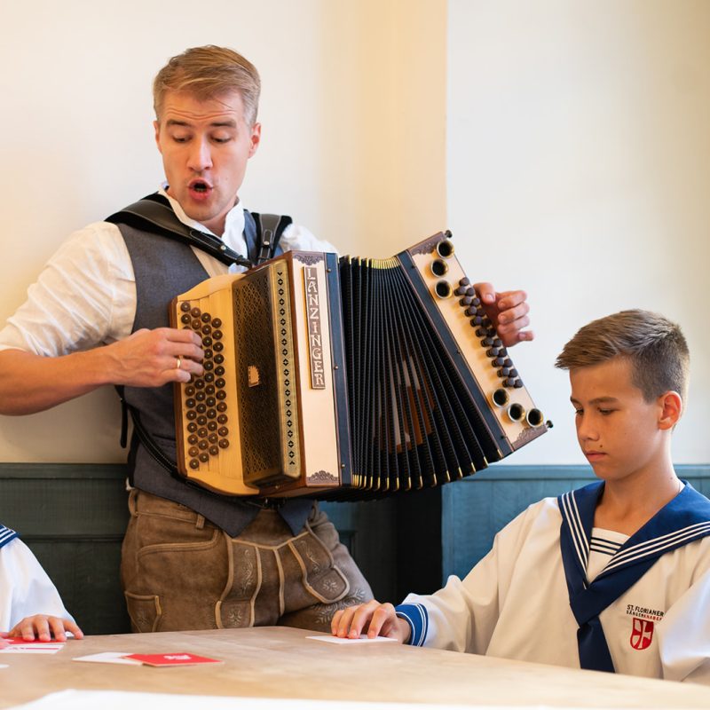 Foto von einem Mann mit steirischer Harmonika und zwei Jungen im Gewand der St. Florianer Sängerknaben