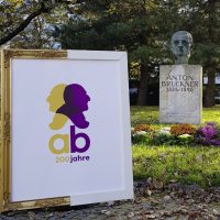 Framed picture with Bruckner double head outdoors in front of an Anton Bruckner monument.