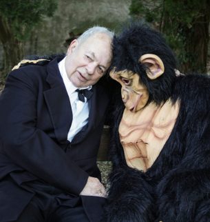 Man in a suit next to costumed monkeys. Both have each other in their arms