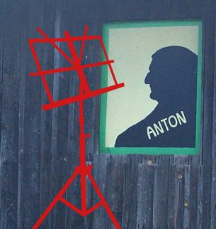 A digitally inserted music stand in red stands in front of a wooden wall, on which an image of Anton Bruckner